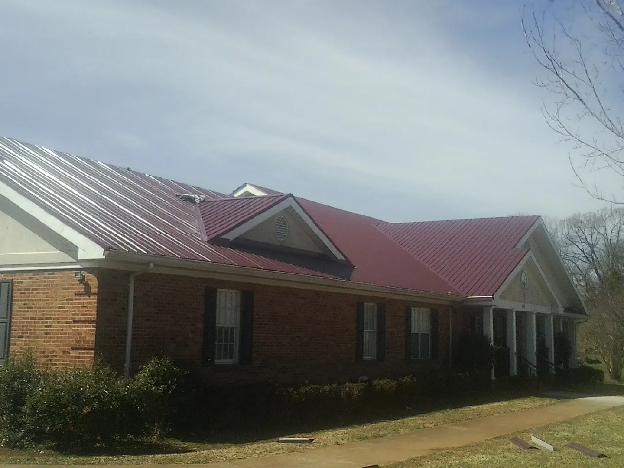 Red metal roof with gabled entries on a long brick building, from a Hail Damage Roof Repair job in Gorham