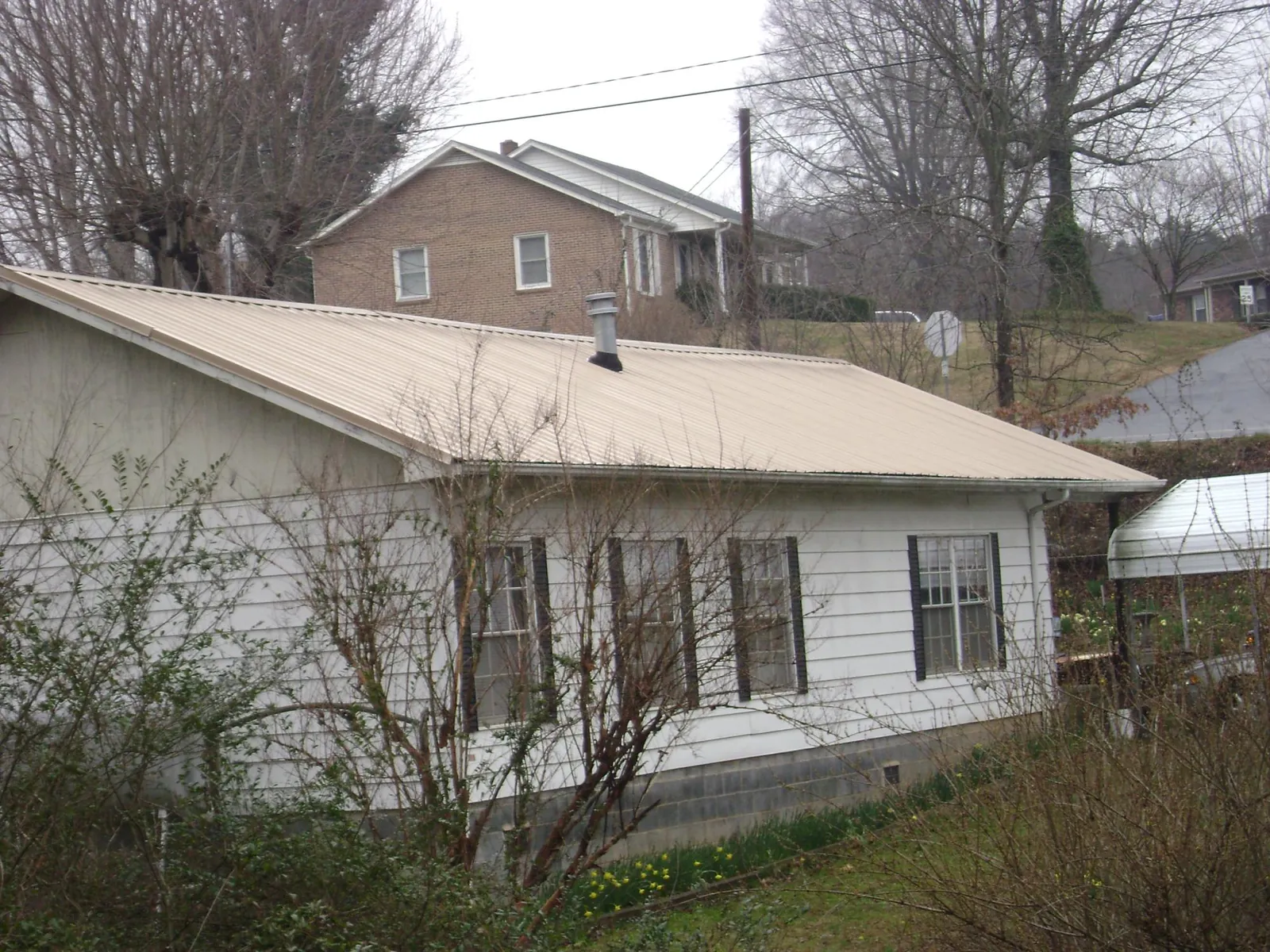 Tan metal roof on a white sided house set into a hillside — Commercial Roofing by Roofing Brothers in Gorham