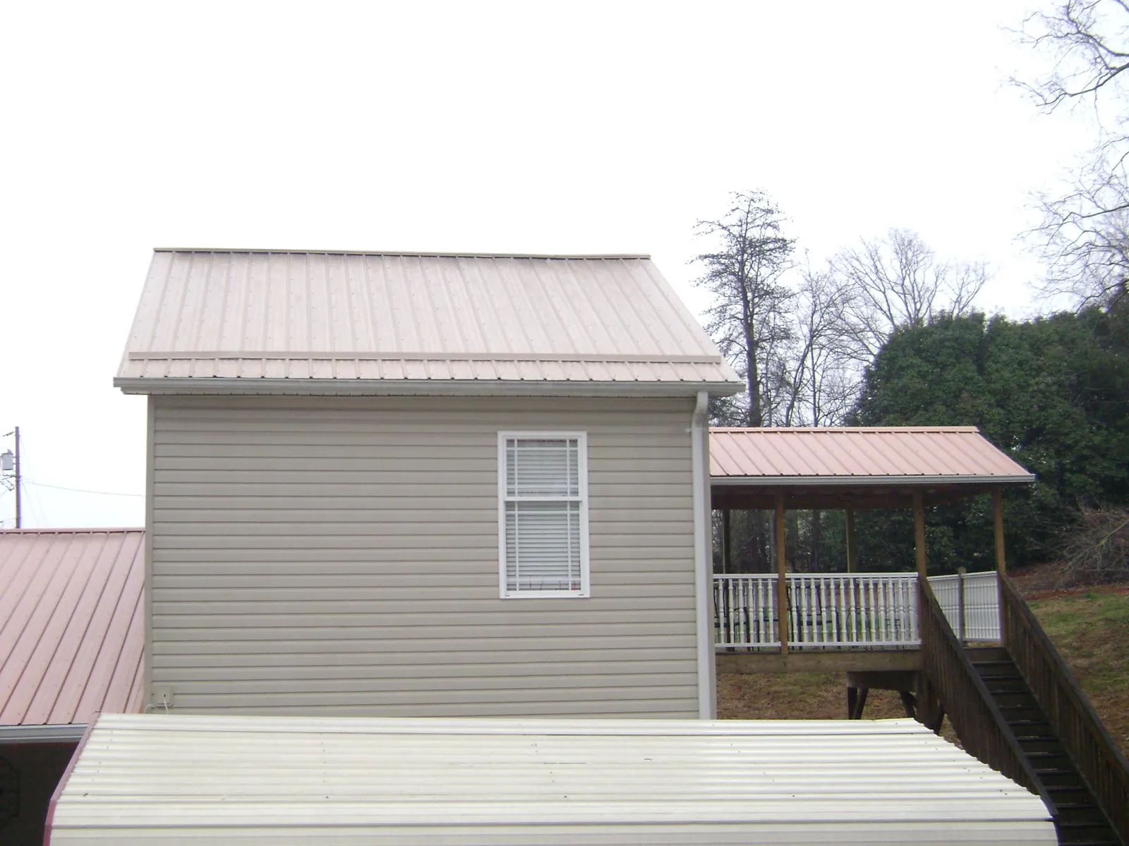 Tan metal roofs on a two story addition and attached porch, from a Roof Replacement job in Gorham